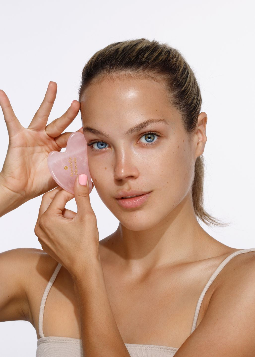 Kobieta prezentująca płytkę gua sha z różowego kwarcu Annabelle Minerals podczas pielęgnacji twarzy
