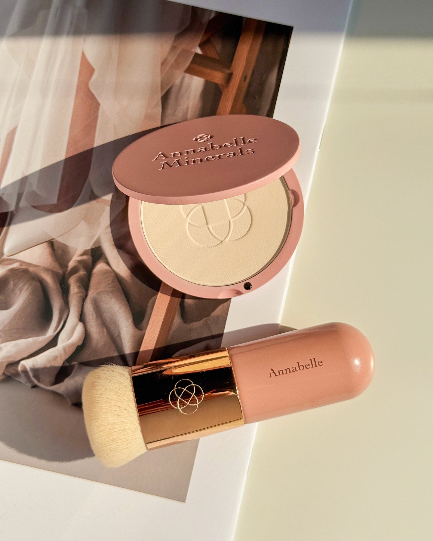 Kompakt mineralnego podkładu Annabelle Minerals z jasnym odcieniem i pędzlem short top na tle miękkich tekstyliów