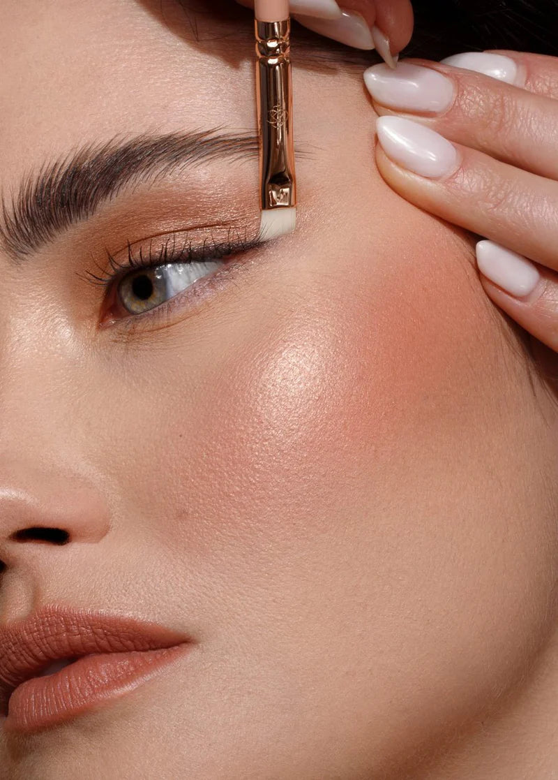 Kobieta nakłada makijaż, używając pędzla do eyelinera Annabelle Minerals, z zadbanymi paznokciami i gładką skórą