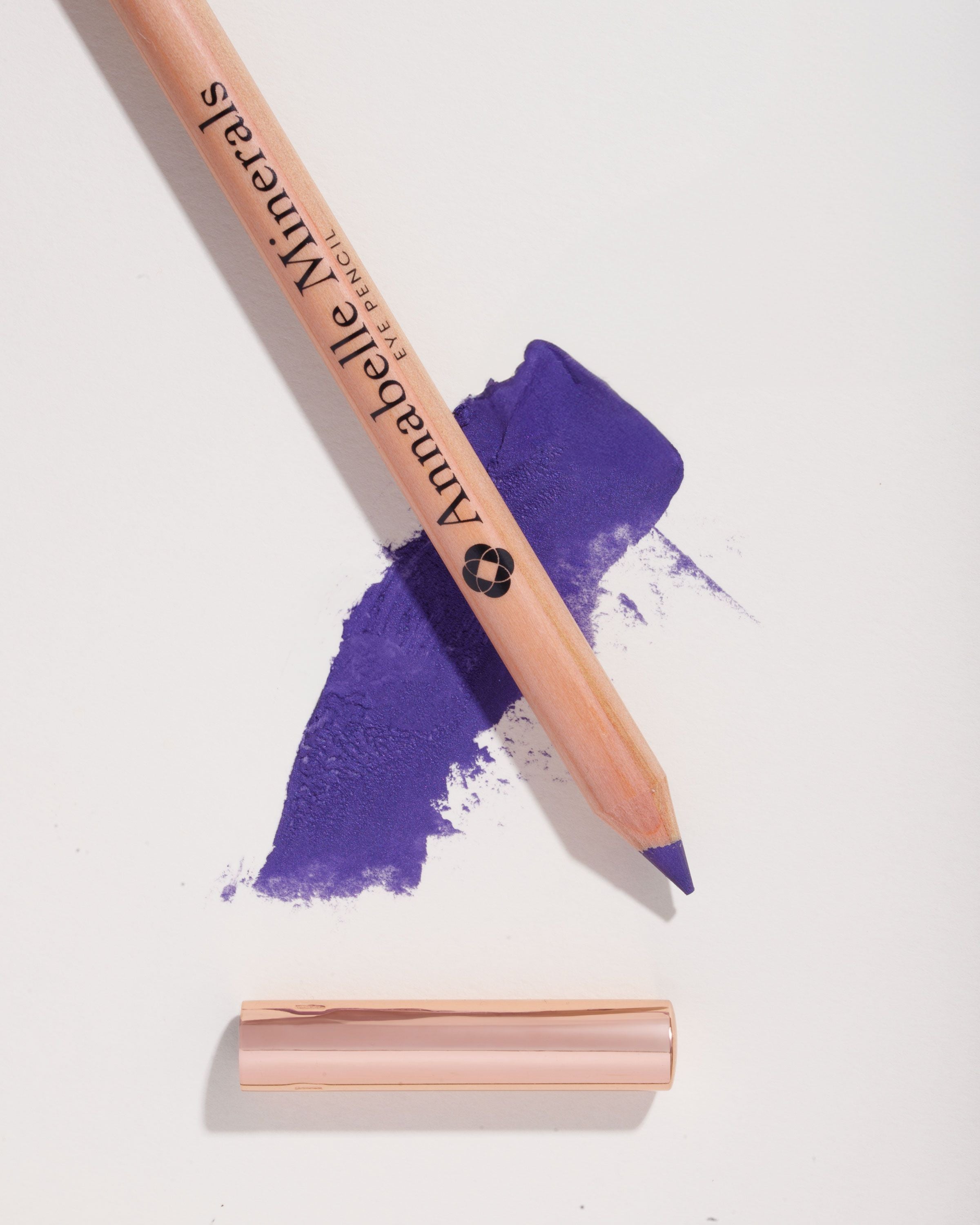 Drewniana, fioletowa kredka do oczu Annabelle Minerals w odcieniu Iris na tle swatcha koloru