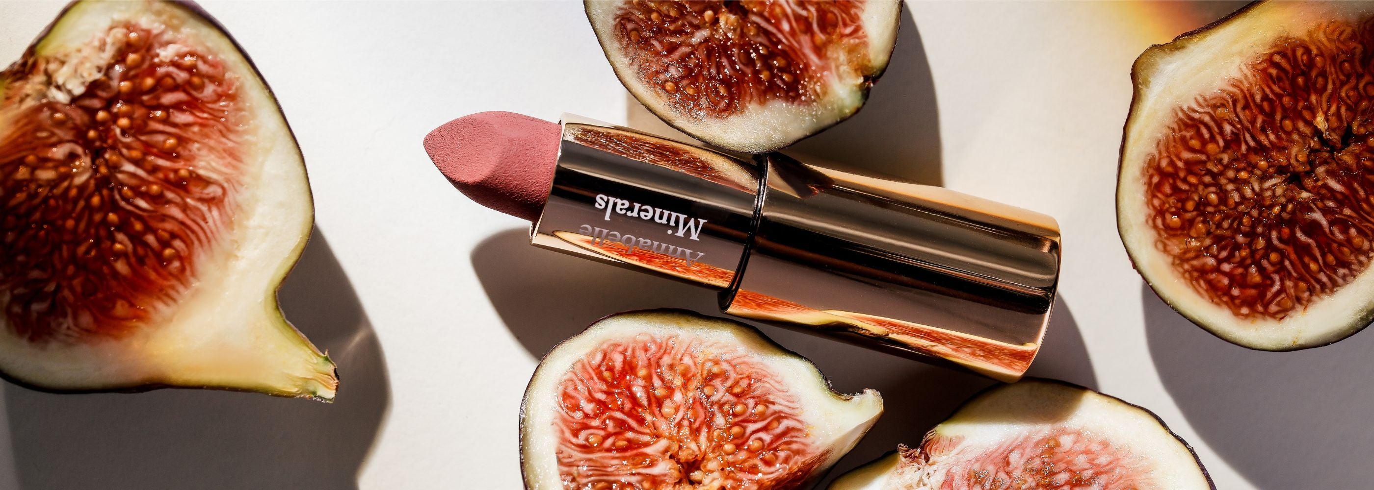 Kremowa, różowo brązowa pomadka Brown Fig Annabelle Minerals w otoczeniu połówek fig