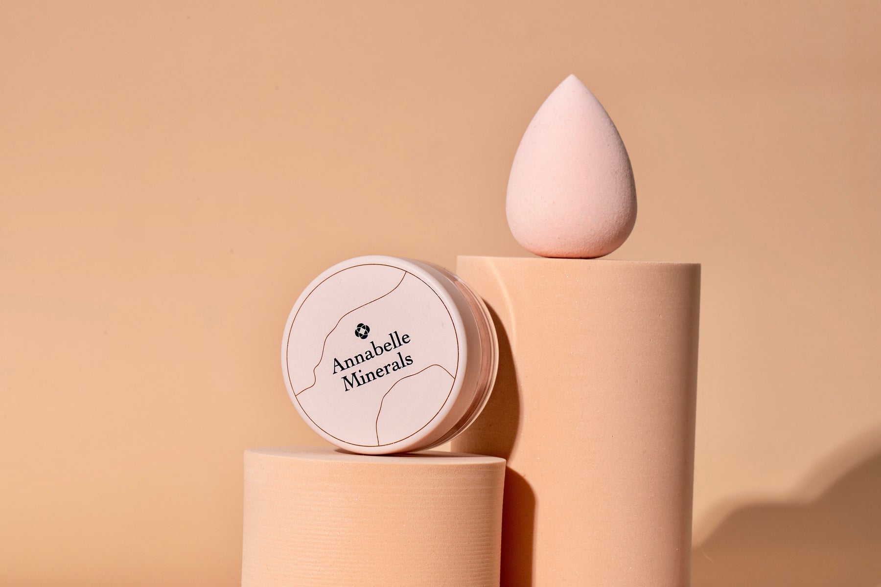Okrągły pojemnik Annabelle Minerals i różowa gąbka do makijażu na cylindrycznych podstawach
