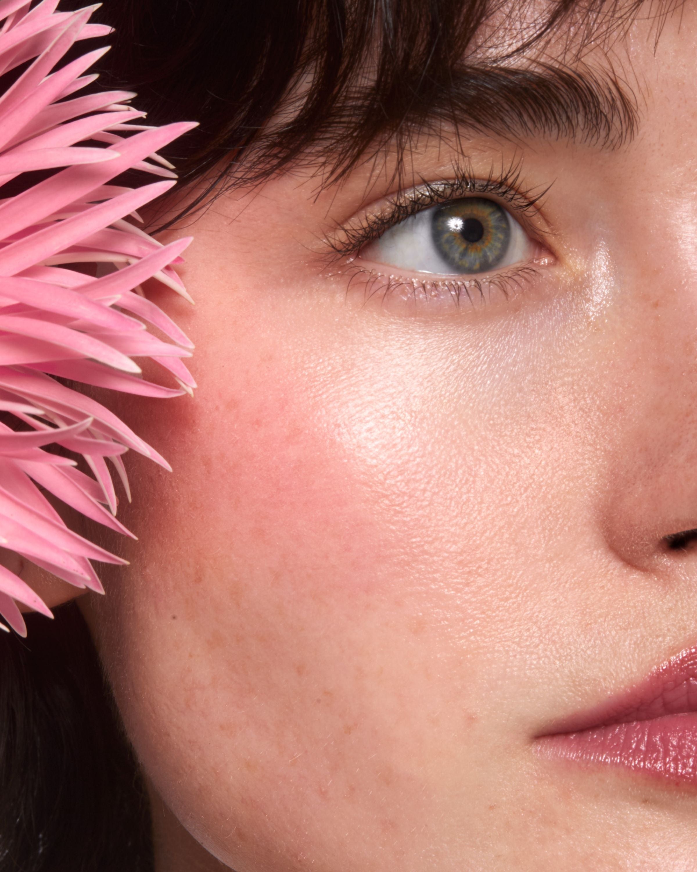 Młoda kobieta z ciemnymi włosami i niebieskimi oczami, z kremowym różem Annabelle Minerals w odcieniu Soft Petal na policzku