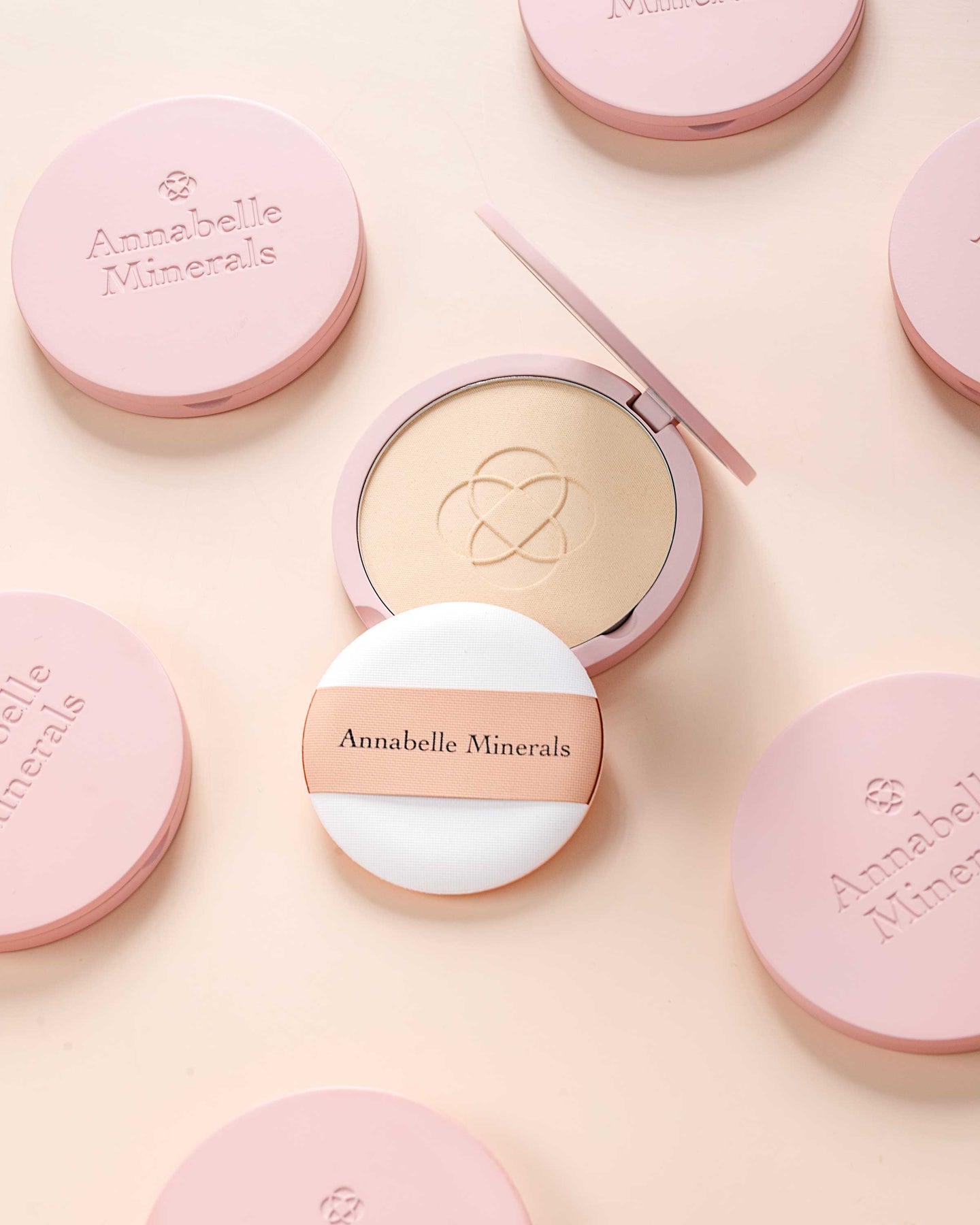 Eleganckie opakowania kosmetyków Annabelle Minerals w odcieniach różu, w tym otwarty podkład prasowany z aplikatorem